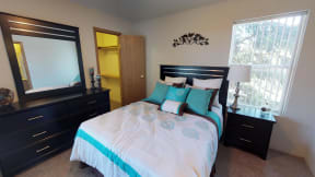 Spacious bedroom staged with a nightstand, bed, and large dresser with walk in closet in view.