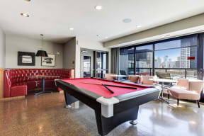 Clubroom furnished with billiards table, cozy seating nook, and a wall of windows looking out to the city.