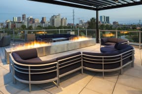 The stylish rooftop features a large outdoor fireplace, comfortable seating, and a pergola all looking out onto stunning skyline views.