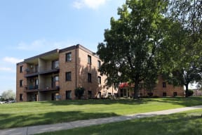 Exterior of Wingate Apartments surrounded by lush grass and large trees.