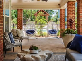 Sitting area in community patio with hanging birdcage chairs, flowers, and cushioned seating