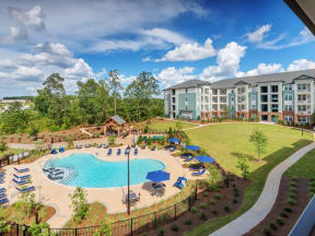 Downward view of pool, sun deck, outdoor sitting area, lawn, and apartment complex