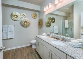 Bathroom with double vanity sink, commode, hard floors, and shower