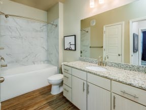 Bathroom with mirror, sink, commode, linen closet, bathtub with marble style walls, and hard floors