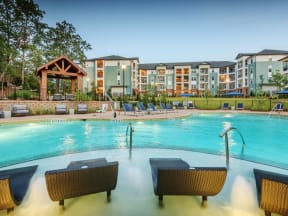 View of the pool entrance and apartment buildings from behind four lounge chairs in the water