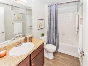 A full-size bathroom with a large mirror, sink, cabinet space, commode, bathtub, and hard floors