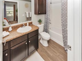 Full-size bathroom with a sink, a mirror, hard floors, brown cabinets, a commode, and a bathtub