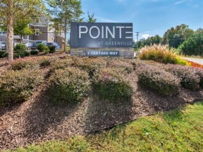Outdoor Pointe at Greenville entrance sign with bushes, grass, and view of the apartments and road