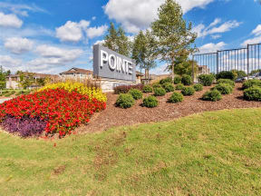 Outdoor Pointe at Greenville entrance sign with bushes, trees, grass, flowers, and apartments