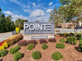 Outdoor Pointe at Greenville entrance sign with bushes, trees, mulch, a car, and parking spaces