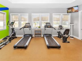 Gym with windows, a TV, scale, elliptical, bicycle, two treadmills and a small crate table