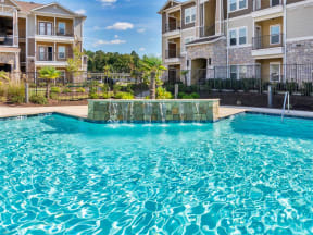 Water fountain splashing into the pool with chairs, trees, and apartments in the back