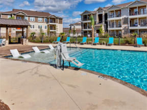 Wheelchair accessible lift in front of the pool, chairs, and gazebo inside gate near apartments