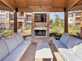 Poolside wooden gazebo with a fireplace, TV, table, and cushioned seating near apartments