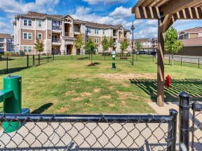Gated dog park with grass, water fountain, pergola, waste station, and street light near apartments