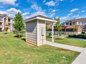 Dog wash station, gated dog park, and grass surrounded by trees, parking garages, and apartments
