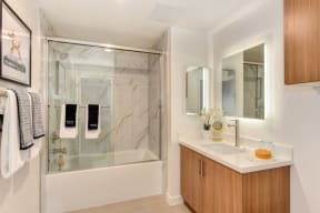 Bathroom with Marble inspired Tub Enclosure, Wood Cabinets, and Mirror