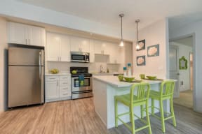Kitchen with Hardwood Inspired Floors, Green Chairs, Refrigerator, White Cabinets and Small White Flower Paintings at Pinecrest Apartments, Davis, California