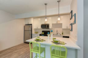 Kitchen with Hardwood Inspired Floors, Green Chairs, Refrigerator, White Cabinets and Small White Flower Paintings at Pinecrest Apartments, California, 95616