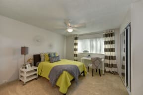 Bedroom with Yellow Comforter Bed, Carpet, Windows, White Table, Beige Chair and Black and White Curtains at Pinecrest Apartments, Davis, CA, 95616