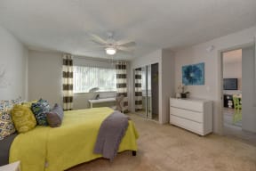 Model Home bedroom with bed in yellow bedding, dresser, and a desk under the window at Pinecrest Apartments, Davis ,95616