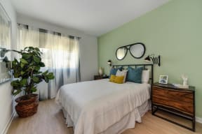 Model home bedroom with light mint green accent wall. Room has queen sized bed and two nightstands on each side of the bed. 