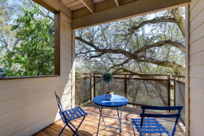 Apartment Patio with blue table and 2 chairs.  There are large oak tree right outside which the branches provide some privacy.