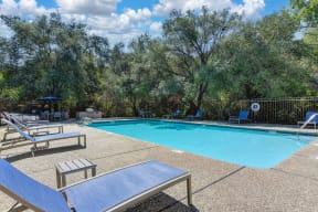One of several swimming pools on-site.  This one is surrounded by oak trees in the distance.  Deck has lounge chairs and tables. 