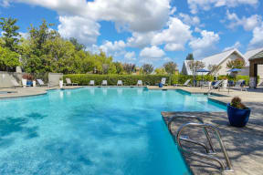 Large swimming pool with lounge chairs around the deck, potted platers and tables & chairs