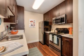 Model Kitchen with Stainless Steel Appliances Dishwasher, Refrigerator, Oven, and Wood Cabinets.