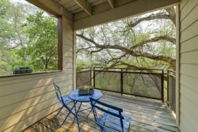 Apartment Patio with blue table and 2 chairs.  There are large oak tree branches that provide privacy.