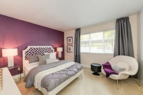 Master bedroom in the model home. Queen size bed with two nightstands. Purple accent wall and plush carpeting on the floors.