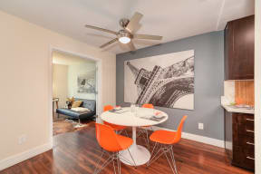 Model Dining area with table and 4 orange chairs.  View of the loft area  in the distance.  Hardwood inspired flooring through out the dining and kitchen area.