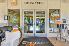 Rental office entrance with two glass doors.  Tables outside the doors and a Renaissance Park door mat outside the doors. 