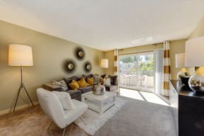 Model living room with plush carpeting, large couch and natural lighting from the patio doors.