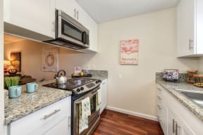 Model home kitchen with granite counter tops, white cabinets and wood flooring.  Kitchen comes with refrigerator, microwave, stove and dishwasher.