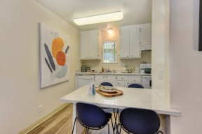 Dining area with white counters and two blue chairs overlooking the kitchen. White cabinets and appliances in the kitchen 
