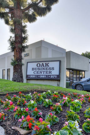 Oak Business Center monument sign at the front of the business park with flowers in front of the sign and a mature pine tree behind it. . 