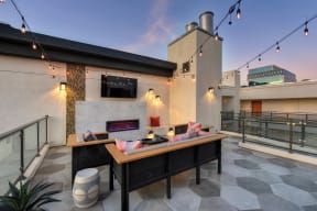 Community rooftop lounge area at dusk.  Area is equipped with chairs, couches, flat screen TV mounted on the wall and views of the city 