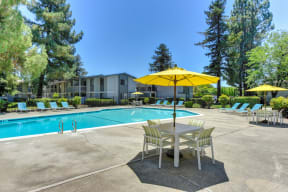 Swimming Pool with Lounge Seating and Tables. Tables have bright yellow umbrellas for shade. 