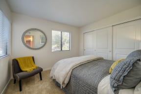 Master Bedroom with gray comforter. Room has Carpet, Gray Chair in corner, large closet with 3 doors and Window