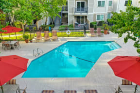 Pool Area with Trees, Red/White/Black Lines Running Down Lounge Chairs and Apartment Exteriors