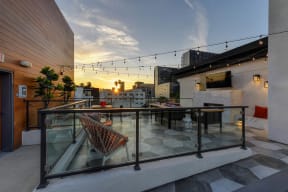 Rooftop lounge area at sunset. Lounge has chairs and couches with fire pit and TV 