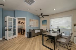 The Legacy Leasing office with large desk and chairs for meeting with prospective renters.  Office has light colored wood flooring and a light blue accent wall.