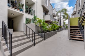 Community grounds and walk path throughout the property.  Several planters with greenery and palm trees.  There are staircases that lead up to the 2nd floor homes along the walkway. 