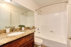 Bathroom with larger vanity with granite counters, darker colored cabinets and tub/shower enclosure with curved curtain rod. 