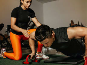 a young woman spotting while a young man does push ups in a gym