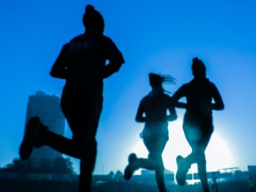 Silhouette of three runners on a city trail with a high rise building in teh background