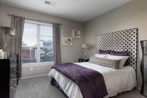 City Place at Westport - Fully Furnished Bedroom With Cozy Bed, Dresser, Carpet Flooring, and a Window With Blinds and Curtains