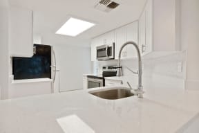 Kitchen with large counter top, sink with vegetable sprayer, stainless steel refrigerator, microwave, and oven